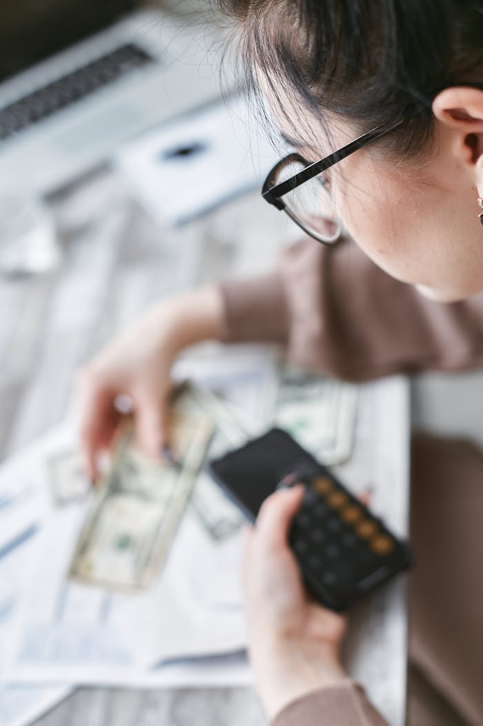 A woman calculates finances using a calculator with banknotes and documents on the table.
